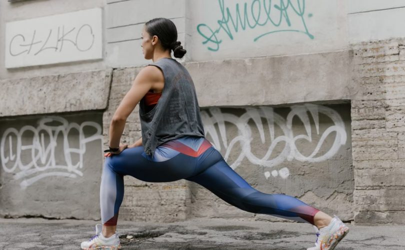 Woman doing lunges for fitness against an urban graffiti wall, showcasing exercise and wellness.